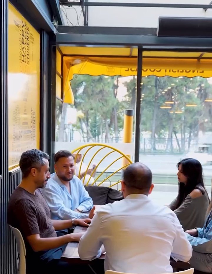 Cam cepheli kafede yetişkinler bir masanın etrafında sohbet ediyor